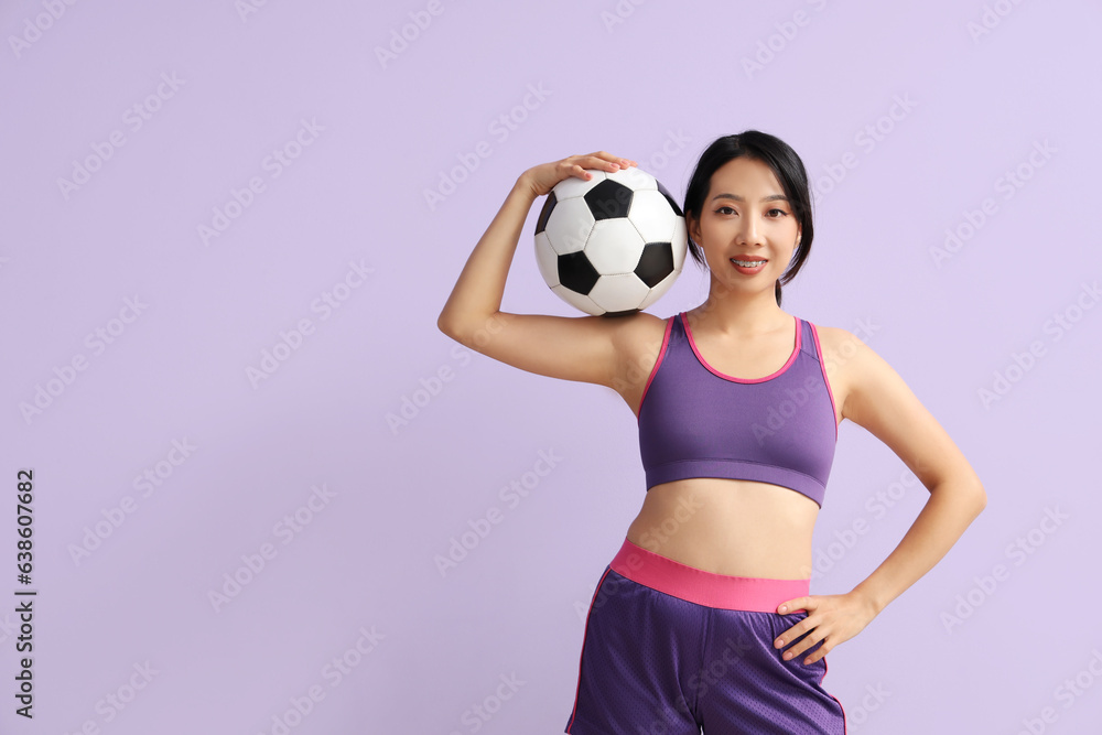 Happy young sporty Asian woman with soccer ball on purple background