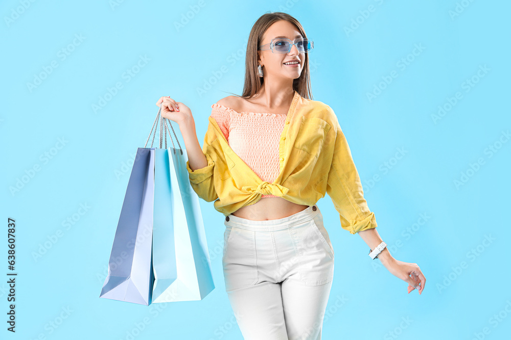 Happy beautiful stylish young woman in sunglasses with shopping bags on blue background