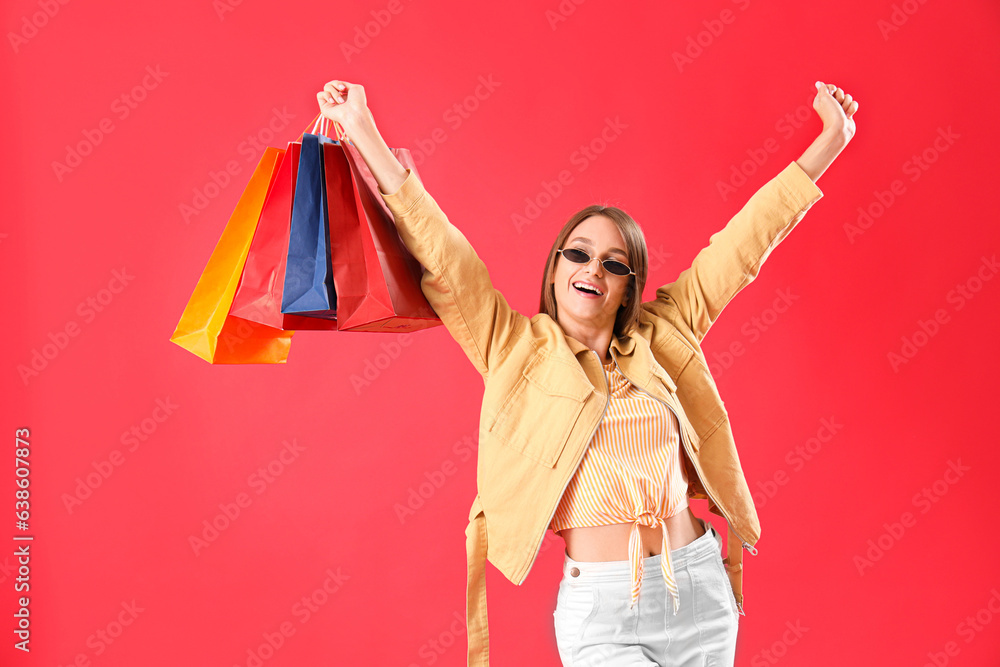 Beautiful happy stylish young woman with shopping bags on red background