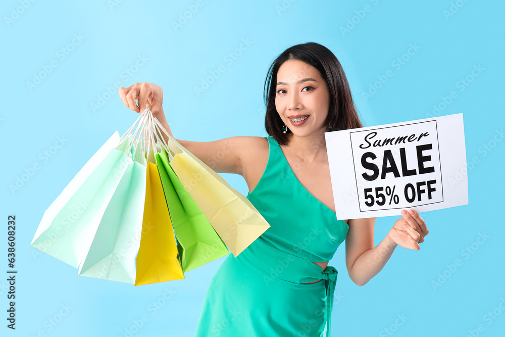 Beautiful stylish young Asian woman with shopping bags on blue background. Black Friday sale