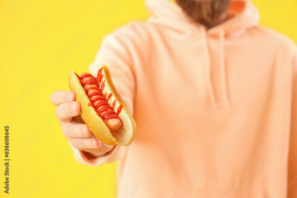 Man with tasty hot dog on yellow background, closeup