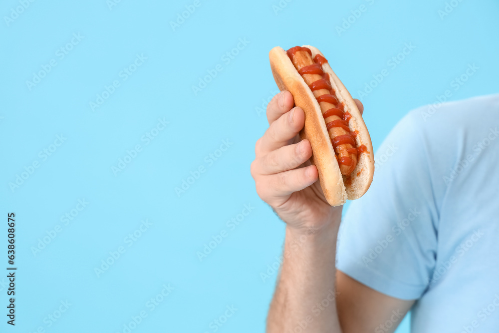 Man with tasty hot dog on blue background, closeup