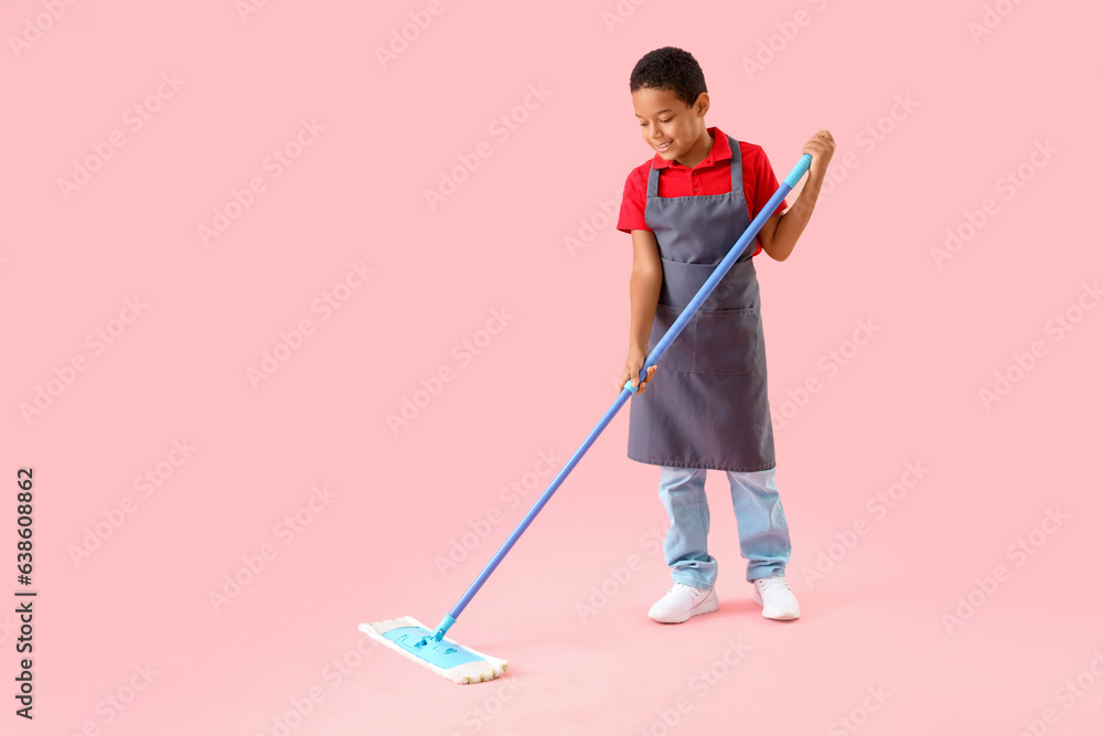 Cute little African-American boy mopping floor on pink background