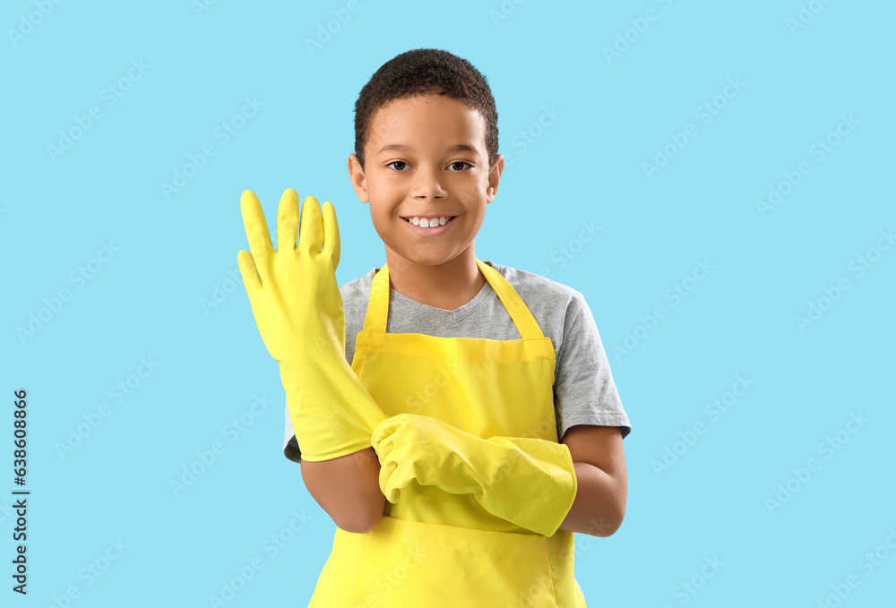 Cute little African-American boy with rubber gloves on blue background