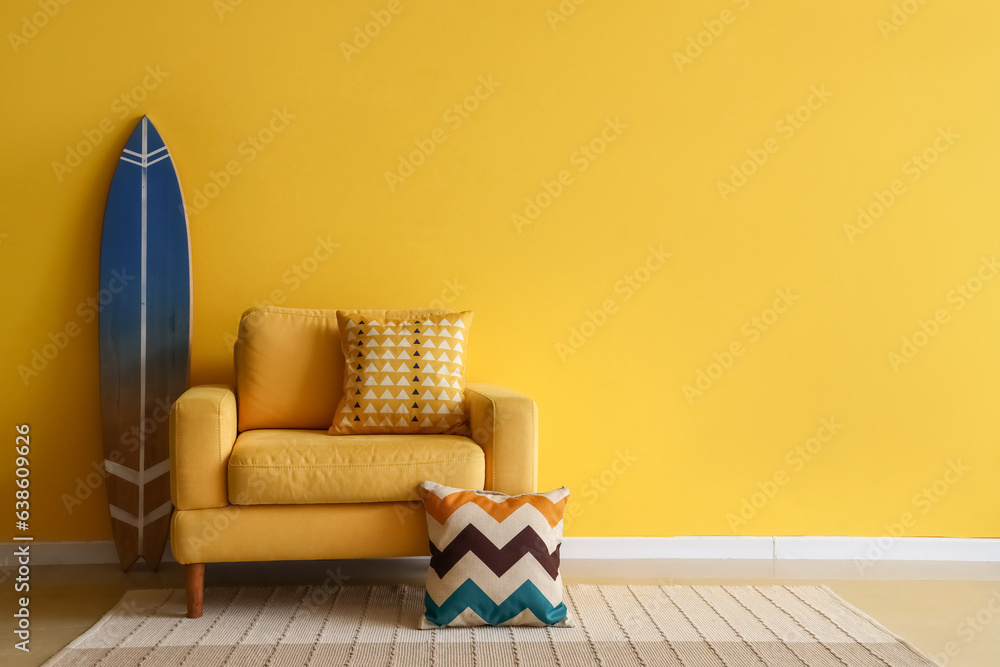 Comfortable armchair and surfing board near yellow wall