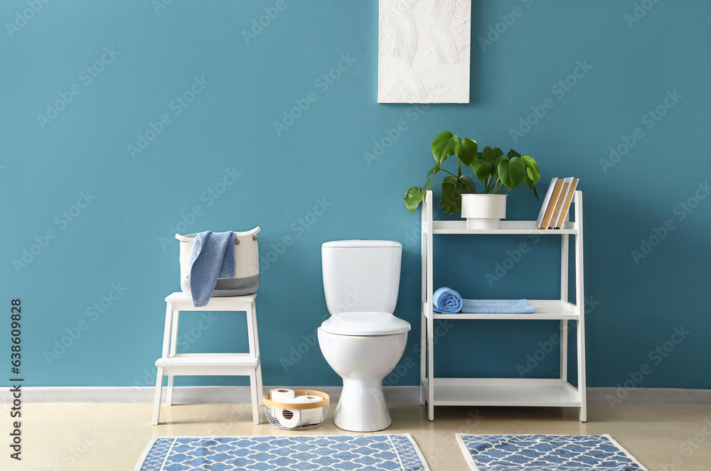 Interior of modern restroom with ceramic toilet bowl and shelving unit near blue wall