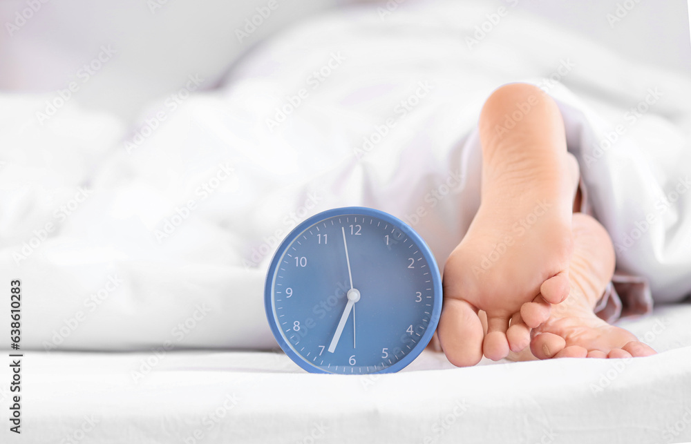 Sleeping womans feet with alarm clock in bed, closeup