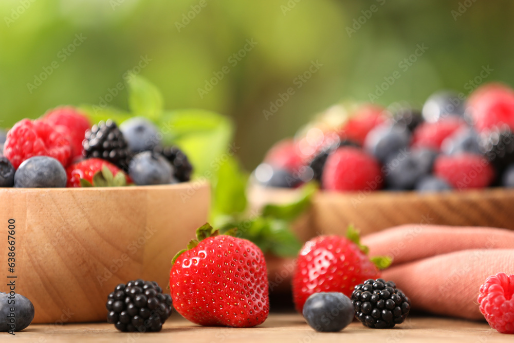 Bowls with different fresh ripe berries and mint on table outdoors, closeup