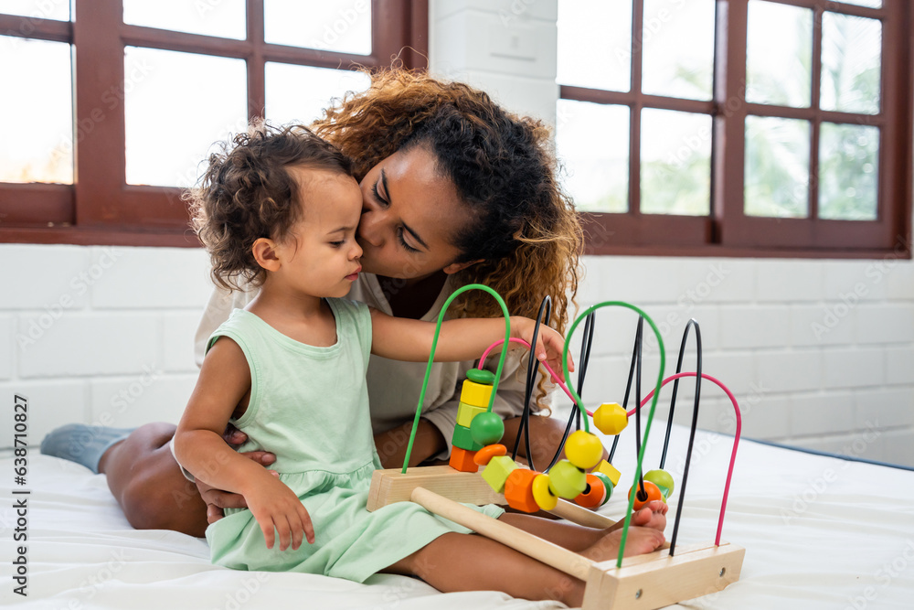 African loving mom play with cute baby girl child on bed in bedroom. 