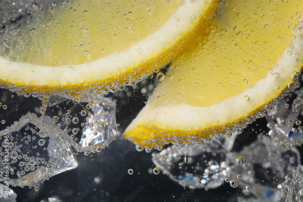 Juicy lemon slices and ice cubes in soda water against black background, closeup