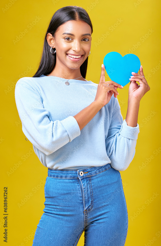 Portrait, smile and woman with blue heart in studio with help, hope or empathy on yellow background.