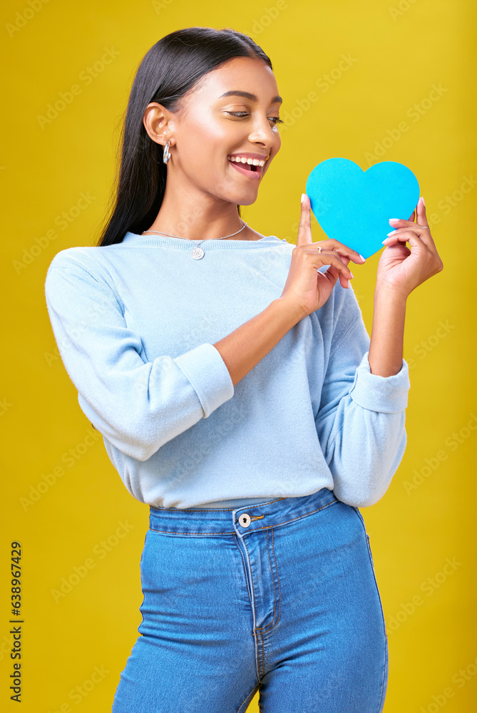 Donation, smile and woman with blue heart in studio for help, hope or empathy on yellow background. 