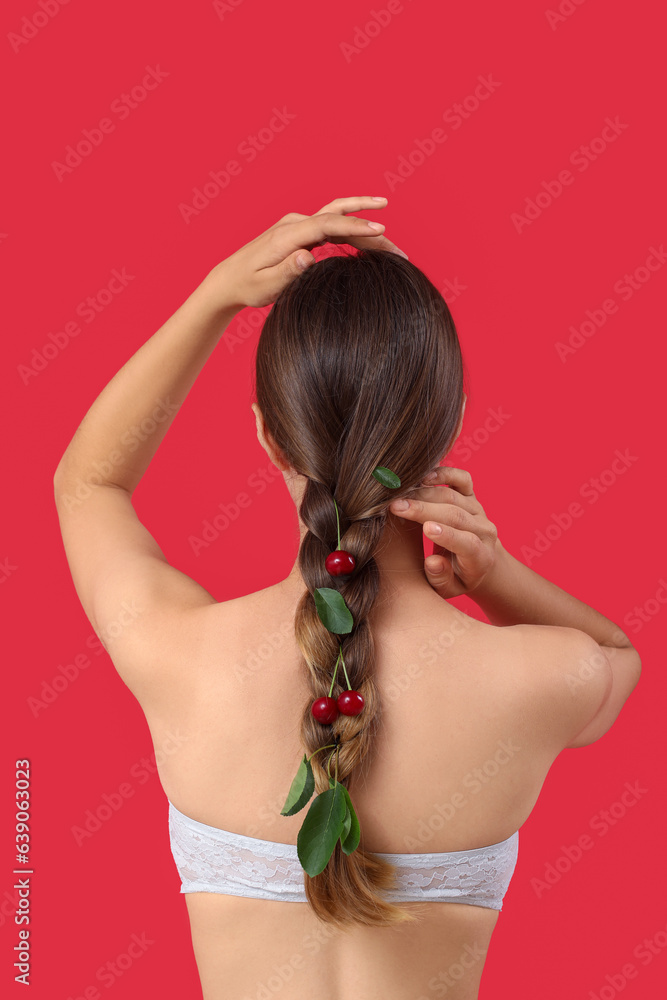 Beautiful young woman with ripe cherries in her hair on red background, back view