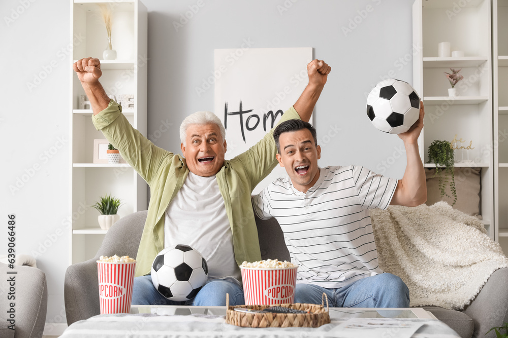 Happy young man with his father watching football game at home