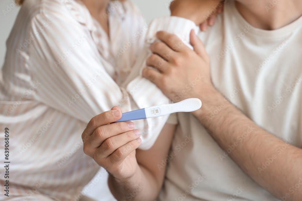 Happy young couple with pregnancy test in bedroom, closeup