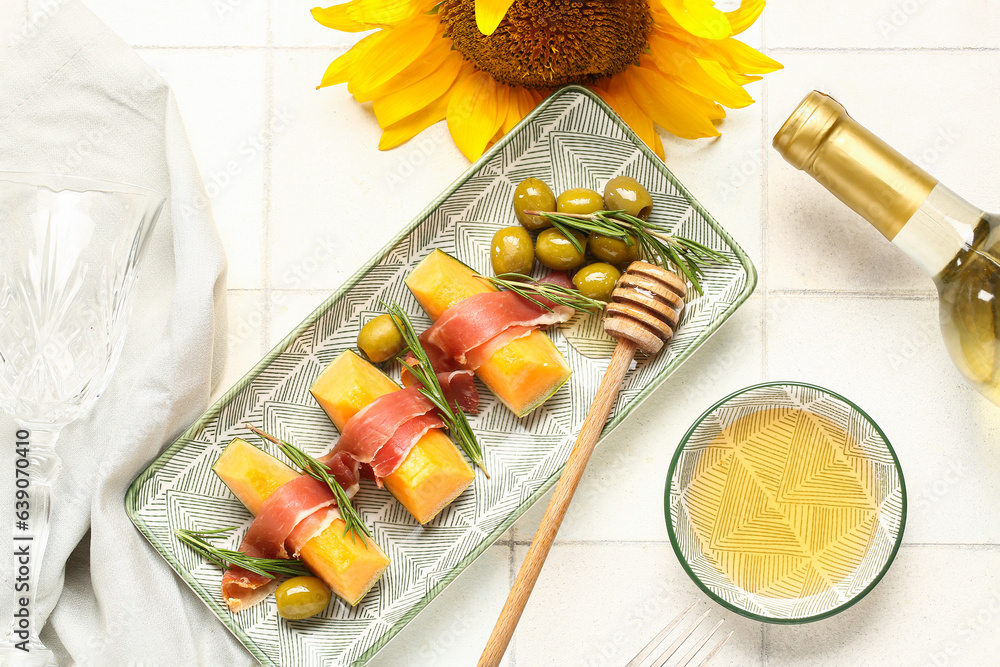 Composition with tasty melon, prosciutto, green olives and honey on light tile background