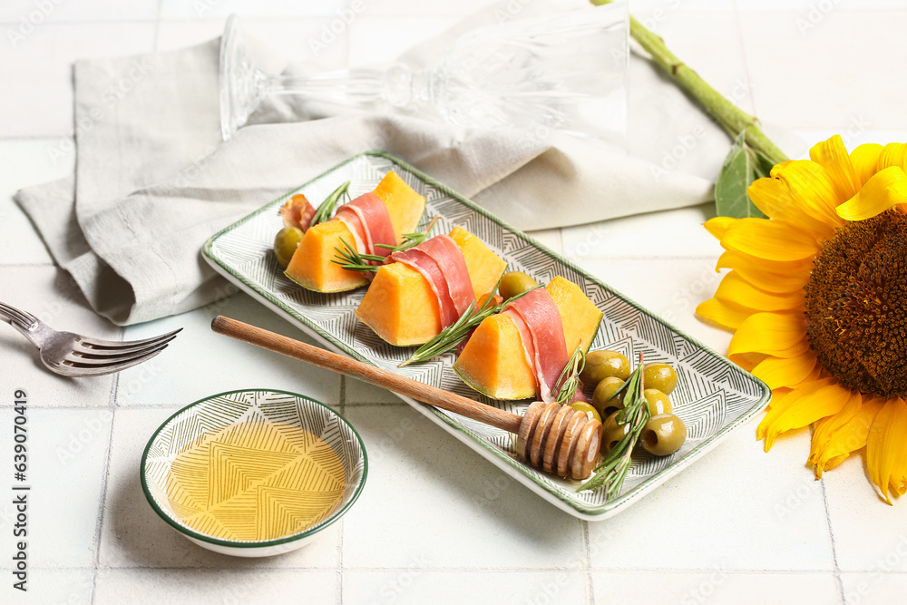 Composition with tasty melon, prosciutto, green olives and honey on light tile background