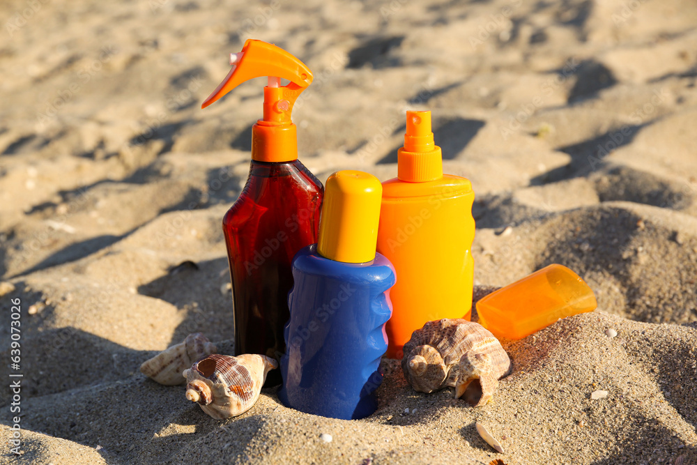 Bottles of sunscreen cream with seashells on sand at beach