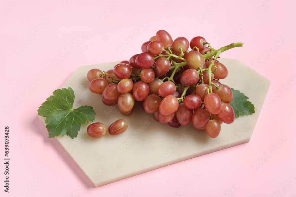 Board with tasty ripe grapes on pink background