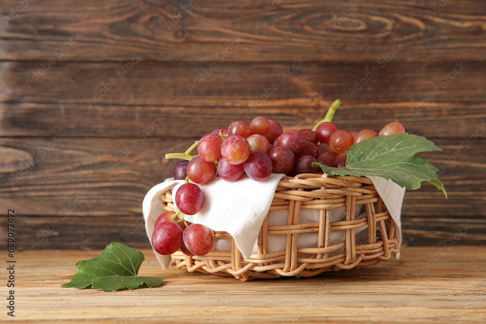 Wicker bowl with tasty ripe grapes on wooden background