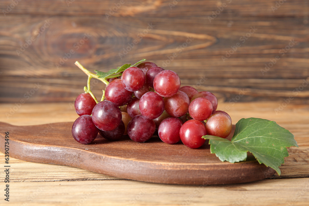 Board with tasty ripe grapes on wooden background