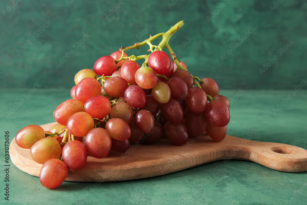 Wooden board with tasty ripe grapes on green background