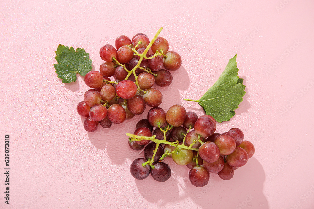 Tasty ripe grapes with leaves on pink background