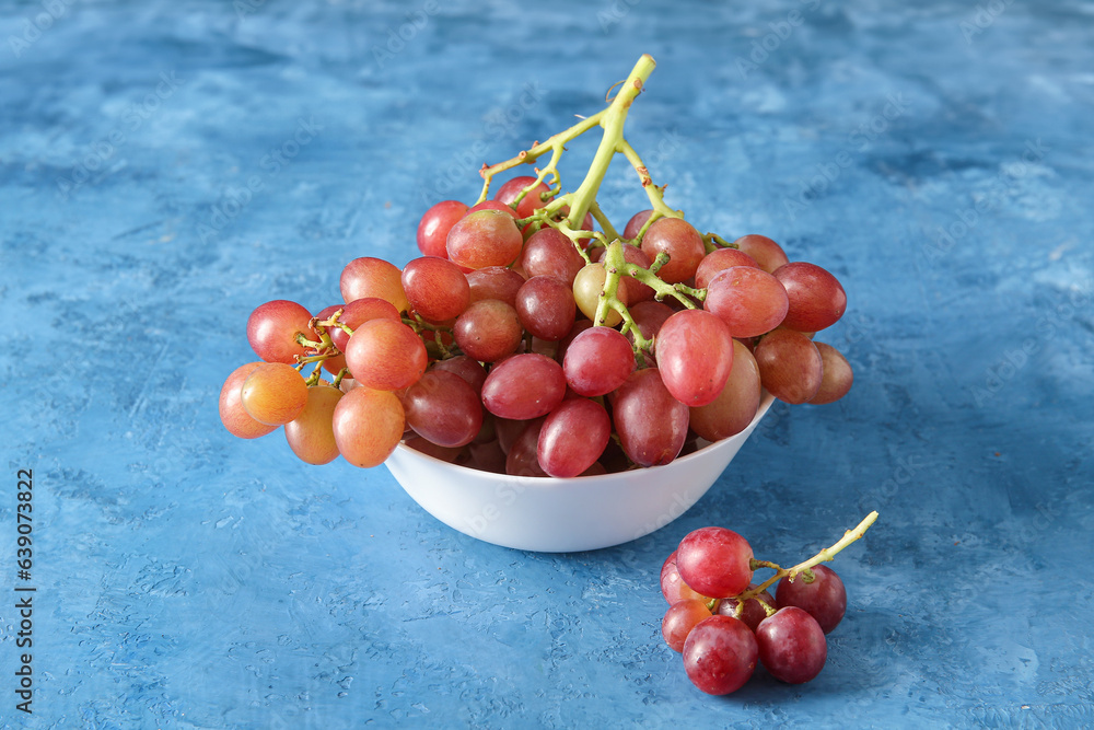 Bowl with tasty ripe grapes on blue background