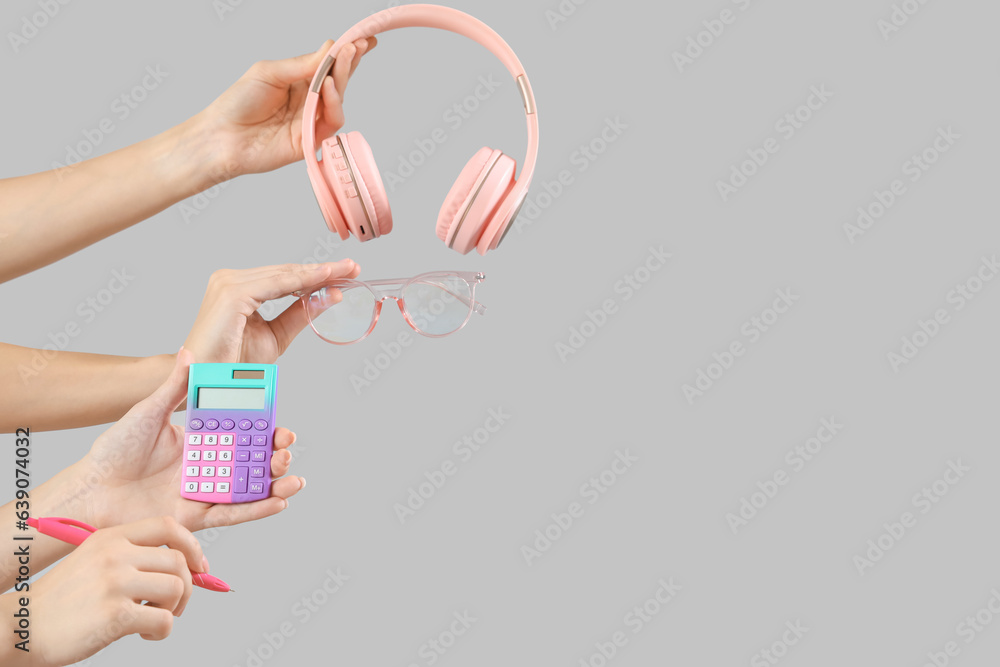 Female hands with headphones, calculator and eyeglasses on grey background