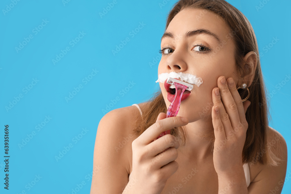 Young woman shaving face with razor on blue background, closeup