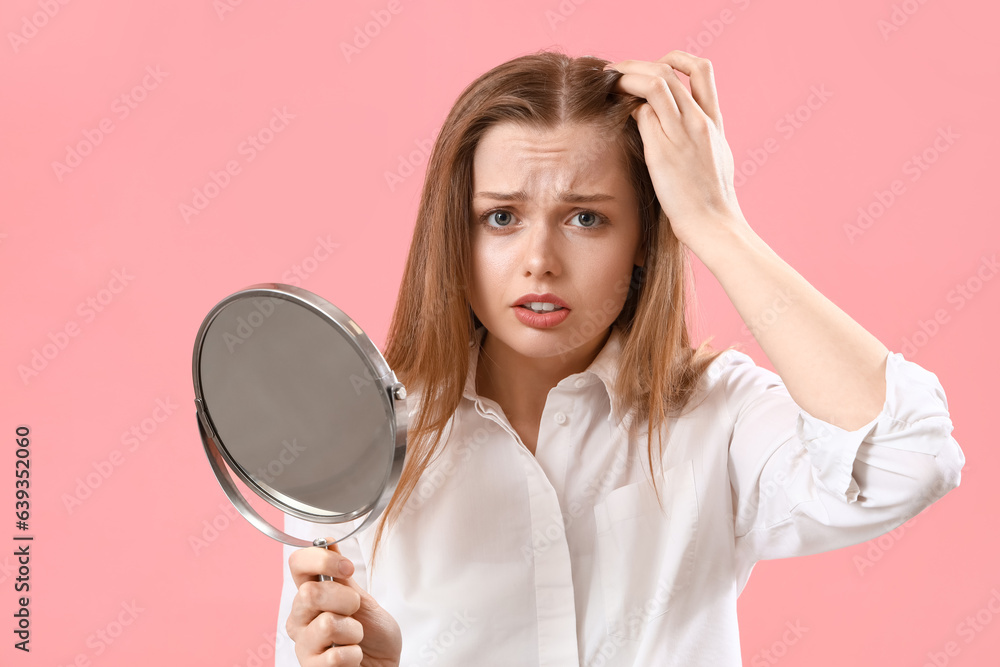 Worried young woman with hair loss problem and mirror on pink background