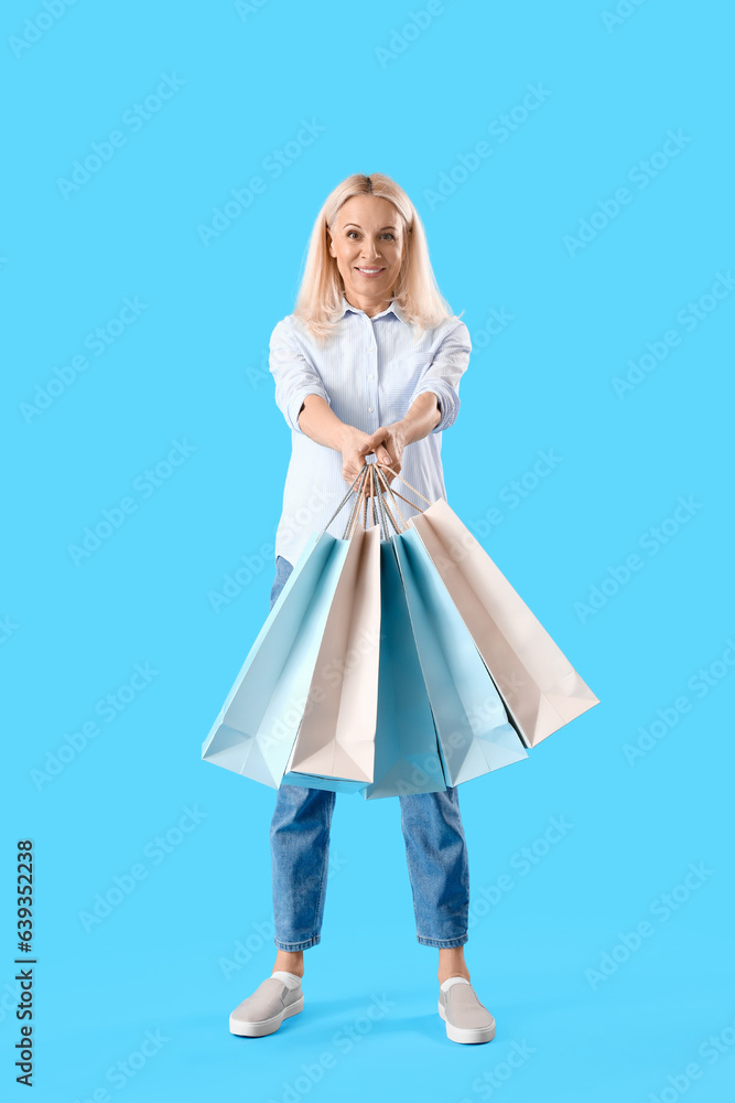 Mature woman with paper bags on blue background. Online shopping