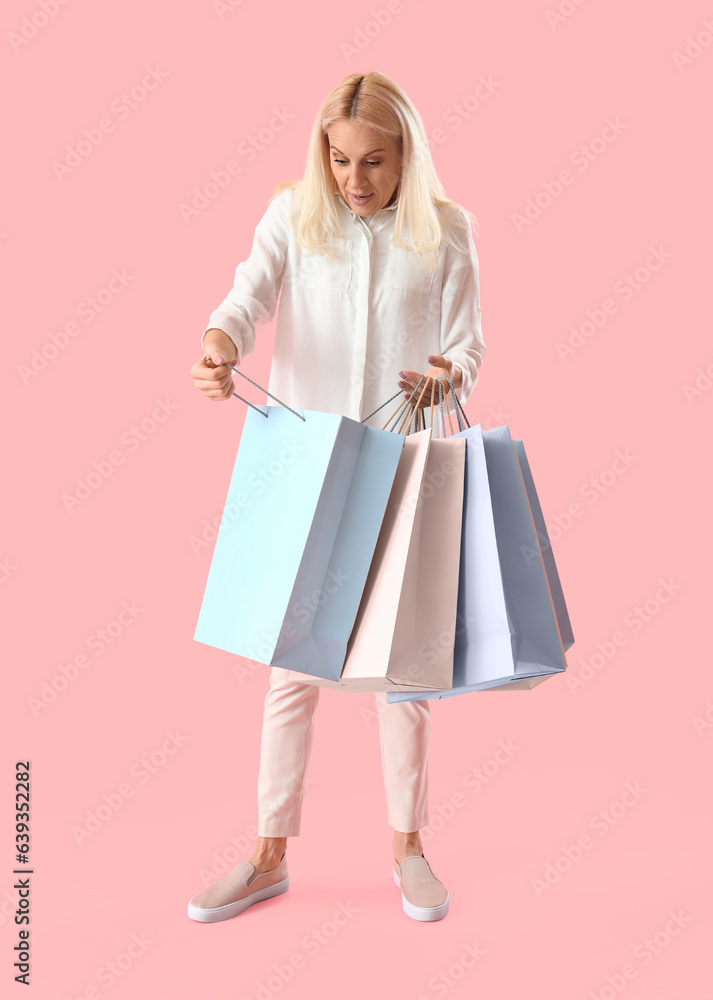 Shocked mature woman with paper bags on pink background. Online shopping