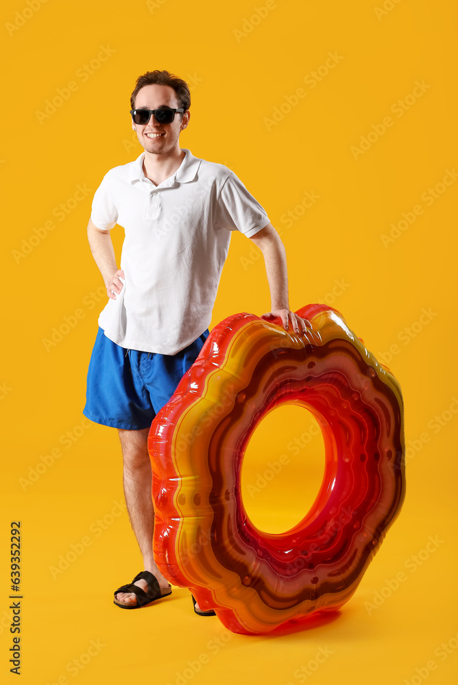 Young man with inflatable ring on yellow background