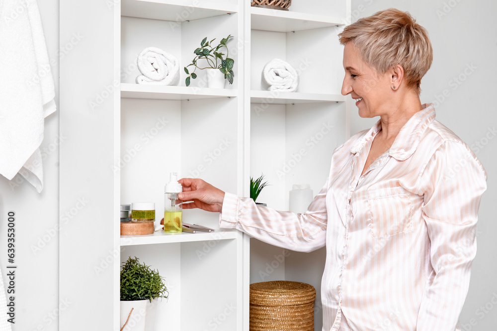 Mature woman taking bottle of cosmetic product from shelf in bathroom