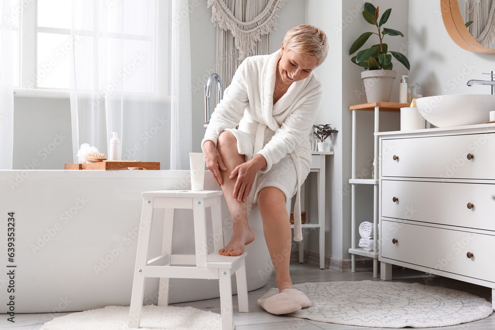 Mature woman applying leg cream in bathroom