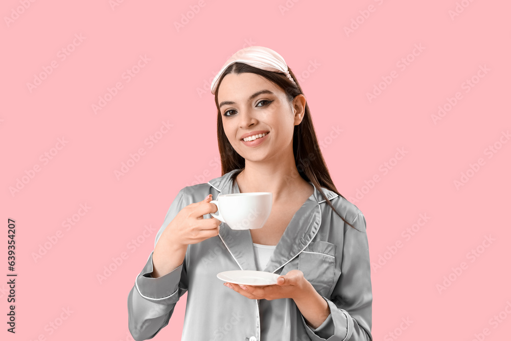 Young woman in pajamas with cup of coffee on pink background