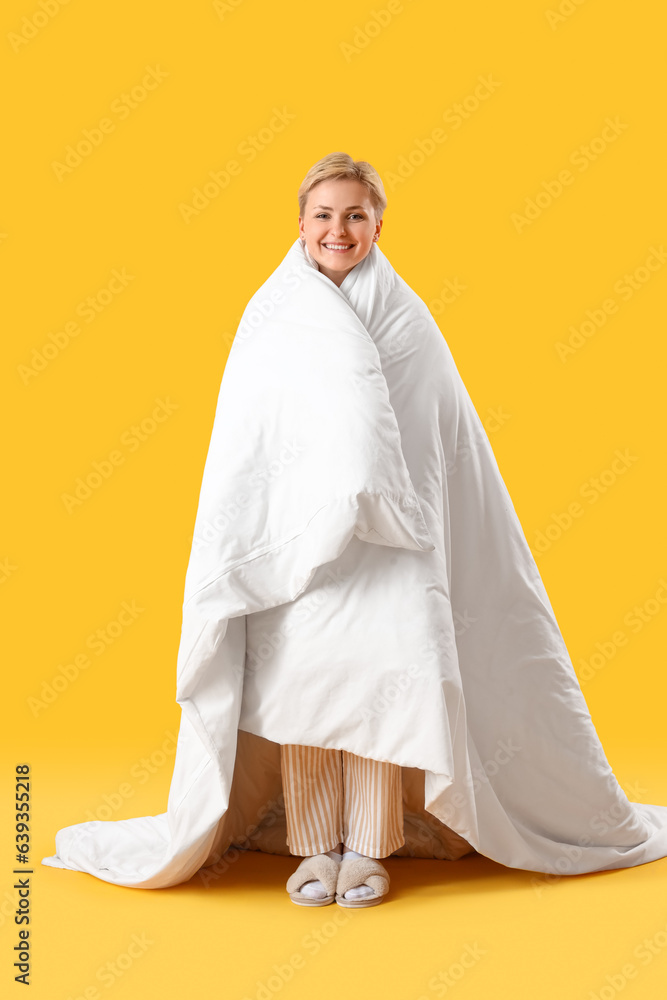 Young woman with blanket on yellow background