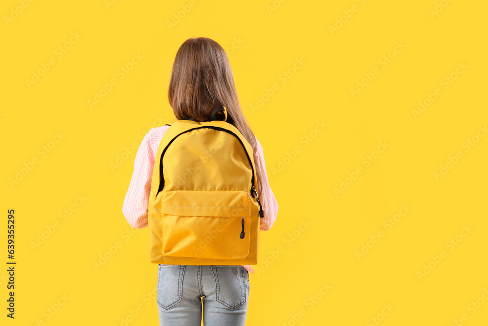 Little girl with schoolbag on yellow background, back view