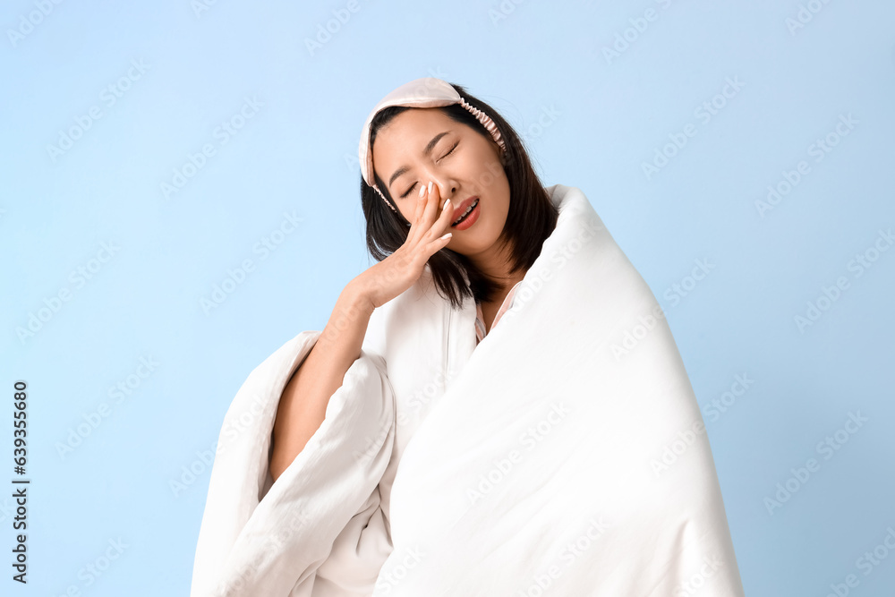 Beautiful Asian woman with blanket on blue background