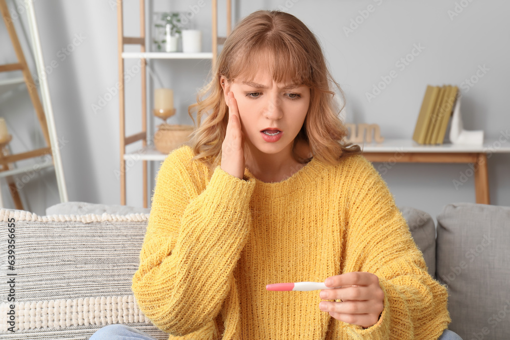 Shocked young woman with pregnancy test at home