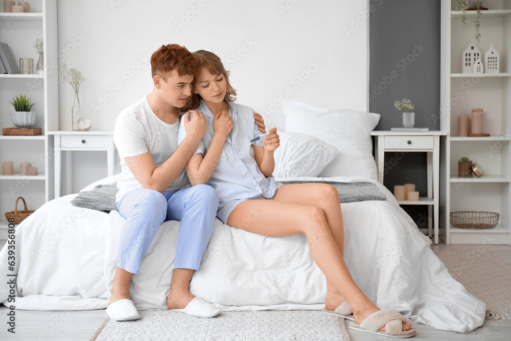 Sad young couple with pregnancy test in bedroom