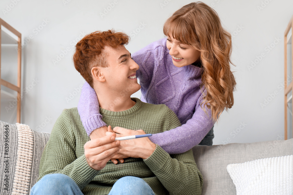 Happy young couple with pregnancy test hugging at home