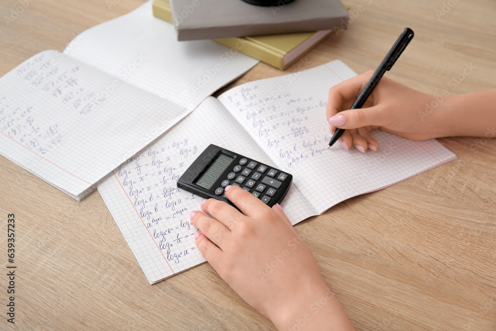 Woman writing math formulas in copybook on wooden table