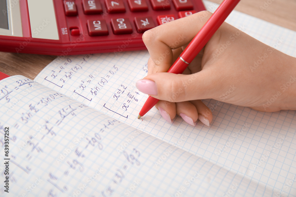 Woman writing math formulas in copybook on wooden table, closeup