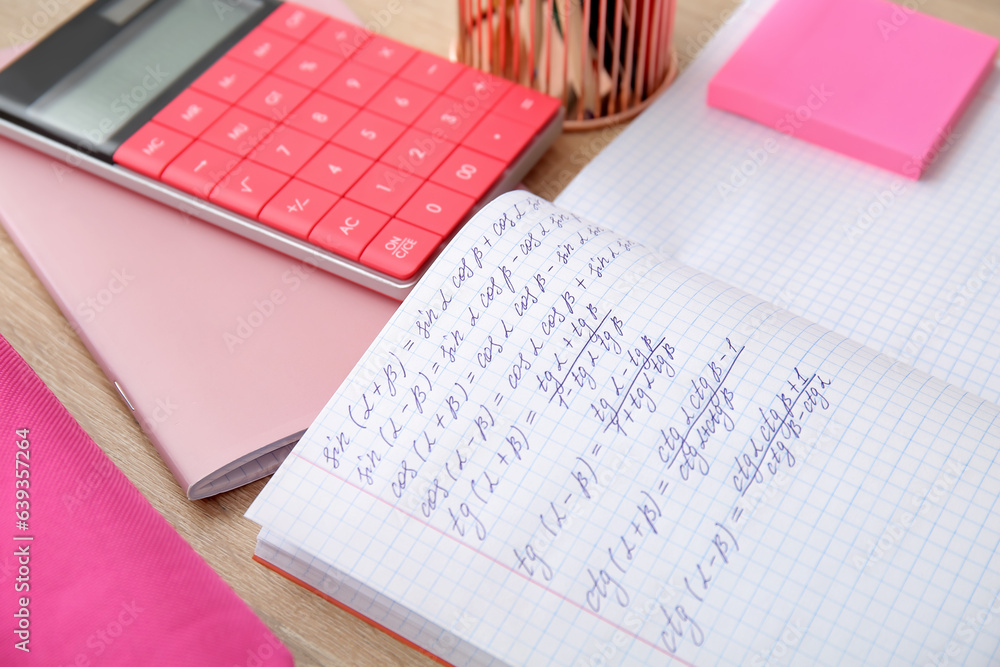 Open copybook with math formulas and stationery on wooden table, closeup