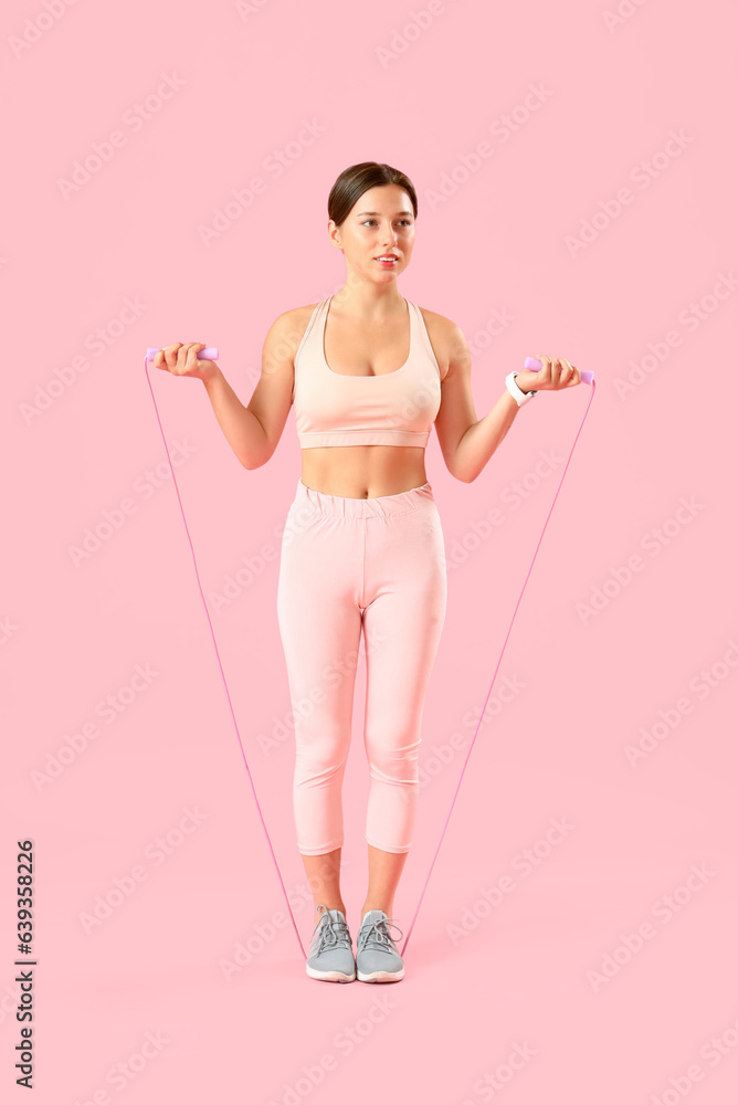 Sporty young woman with jumping rope on pink background