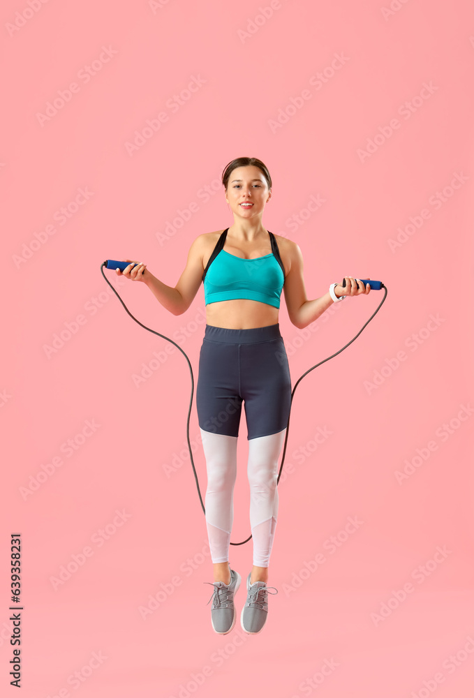 Sporty young woman jumping rope on pink background