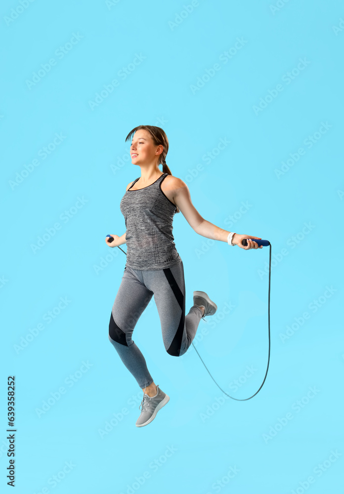 Sporty young woman jumping rope on blue background