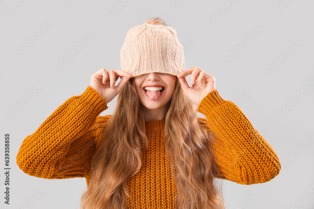 Beautiful young woman in sweater showing tongue on grey background